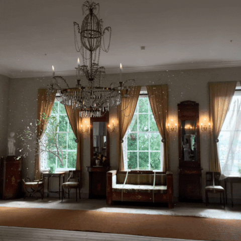 Moving image of an old dining room with a chandelier. Three large windows and a curtain is blowing in the wind.