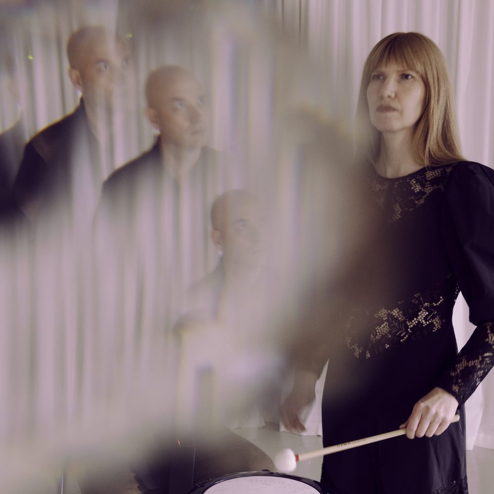 A distorted image of a man looking up at a woman playing a drum.